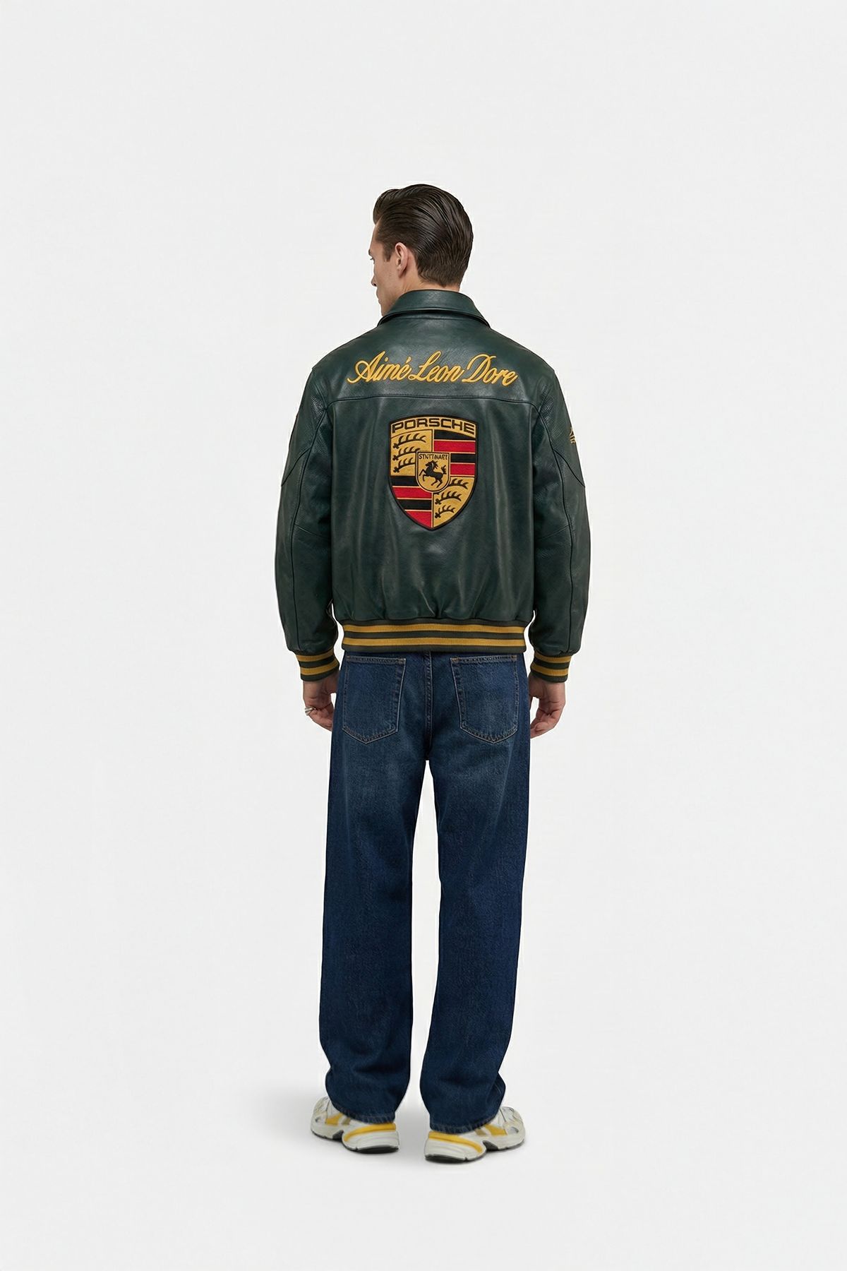 Man wearing a green prosche leather jacket with a logo on the back, standing against a white background