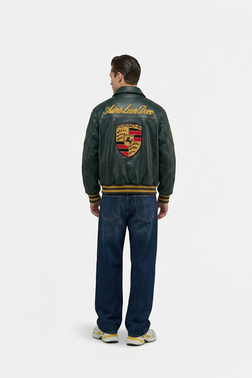 Man wearing a green prosche leather jacket with a logo on the back, standing against a white background