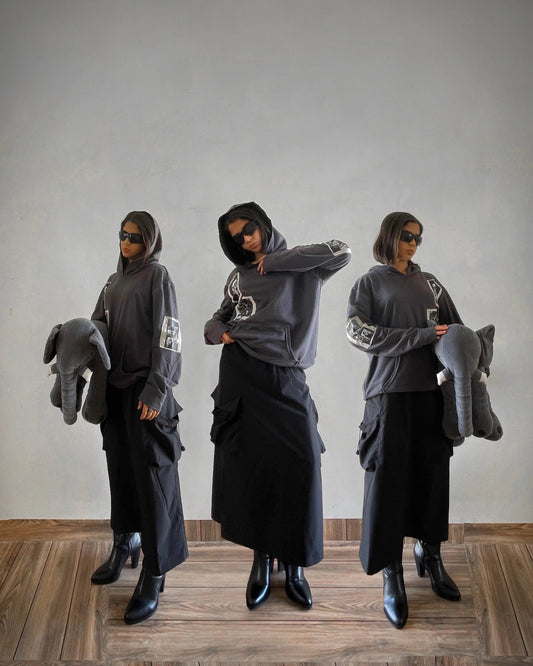 Woman in Y2K streetwear: graphic hoodie, cargo skirt, boots, sunglasses, holding elephant plush