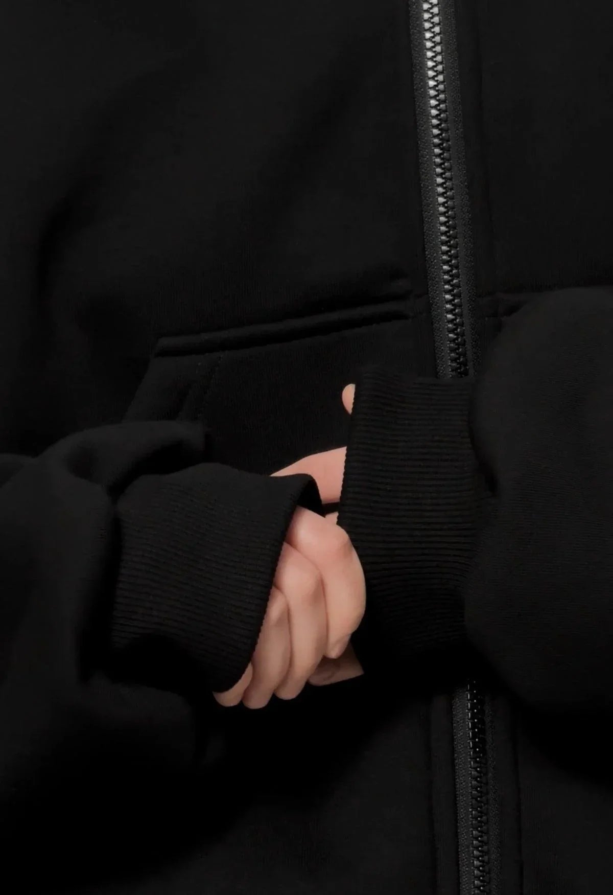 Close-up of hands in oversized black streetwear techwear hoodie with front zipper