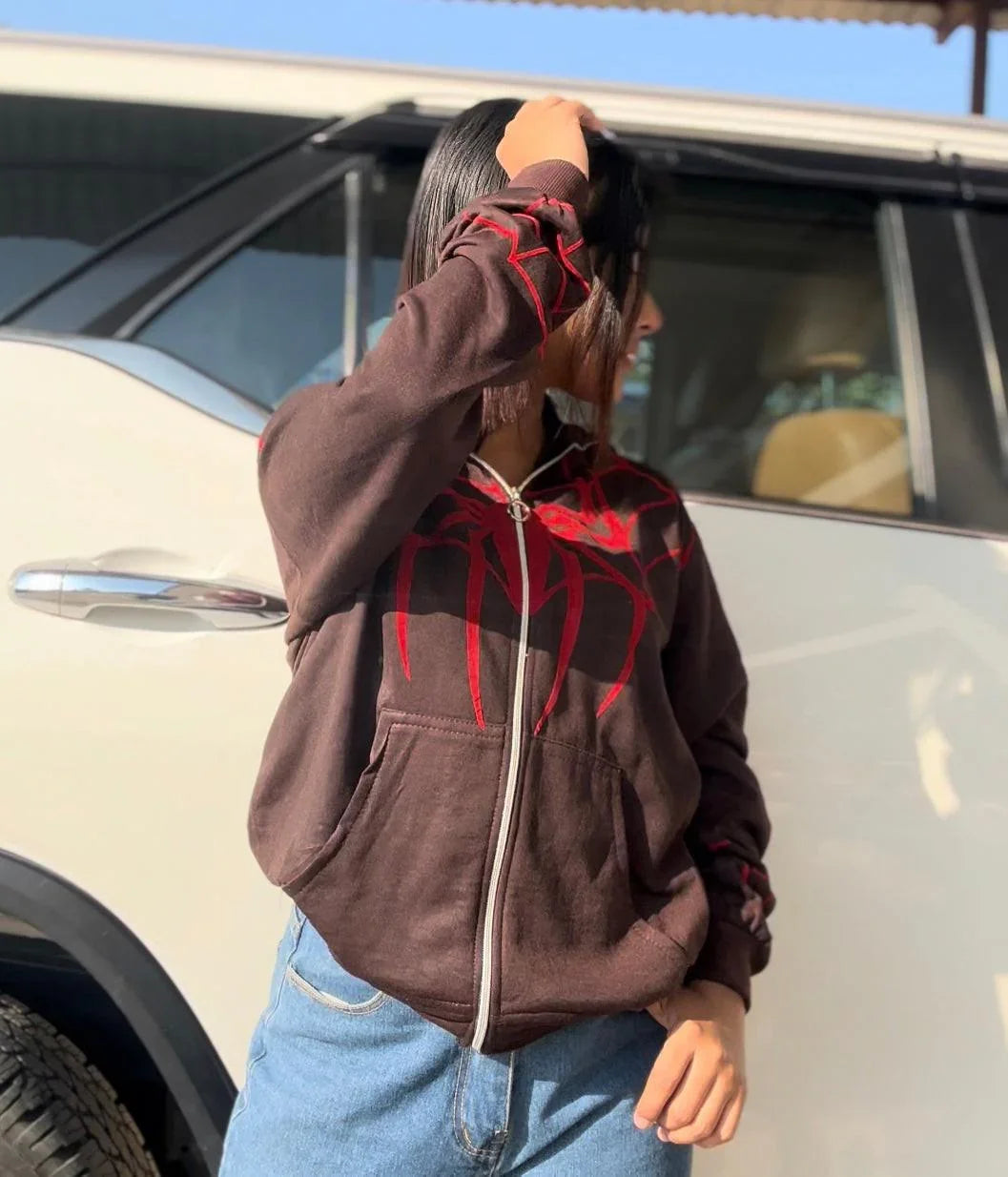 Person wearing brown full zip Spider-Man hoodie with red graphic, casual streetwear style