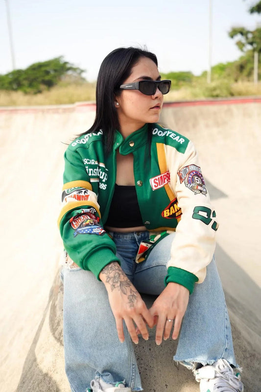 Woman in green and white vintage racer jacket with patches, wearing sunglasses and jeans outdoors